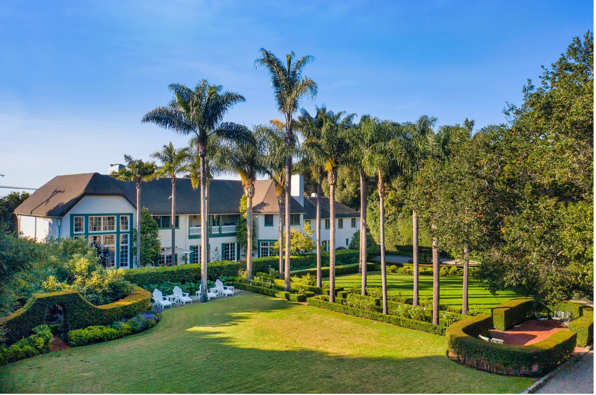 A  very large ocean view home with a green lawn and row of tall palm trees in front