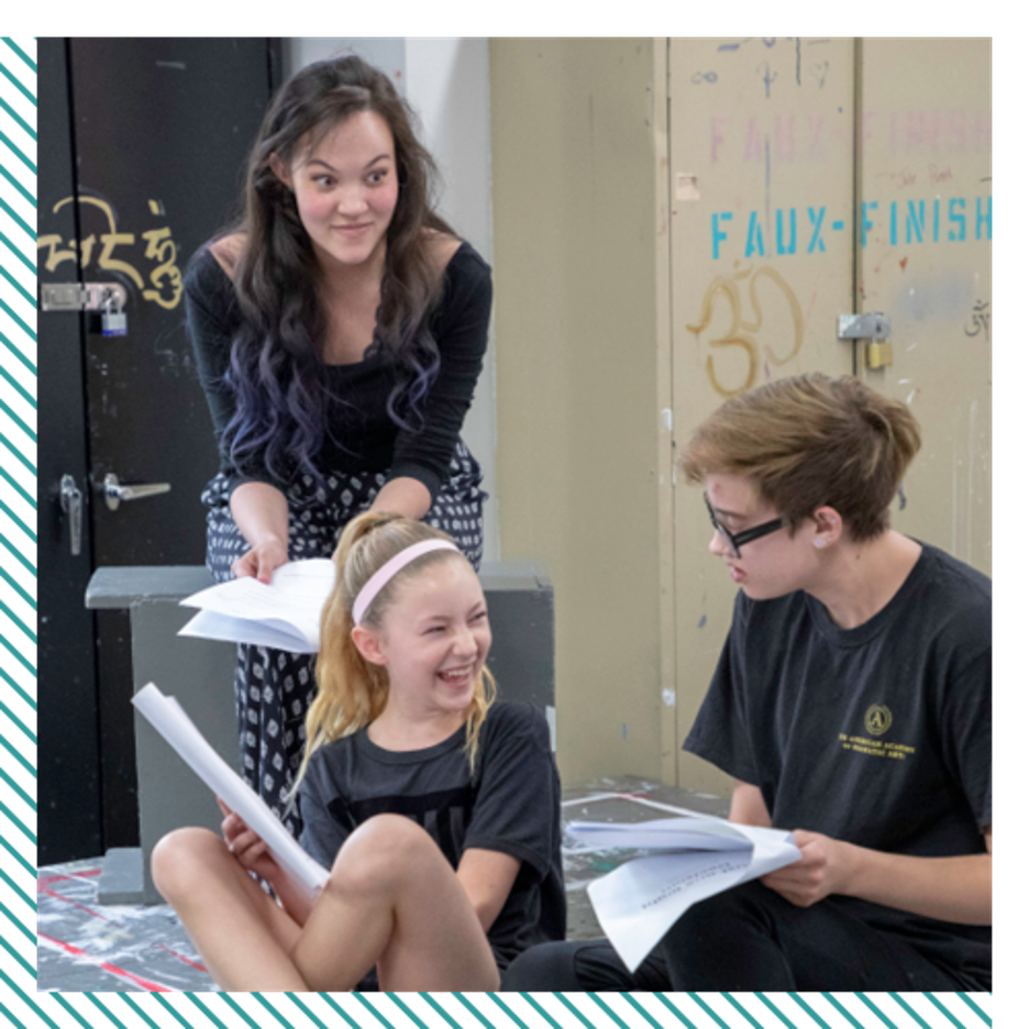 A young woman, a pre-teen boy, and a teenage girl on a set with scripts in their hands.