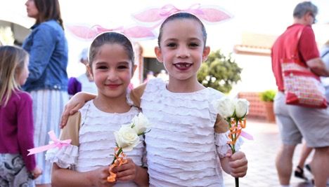 Two young ballerinas with their hair pulled back and roses in their hands following a performance.