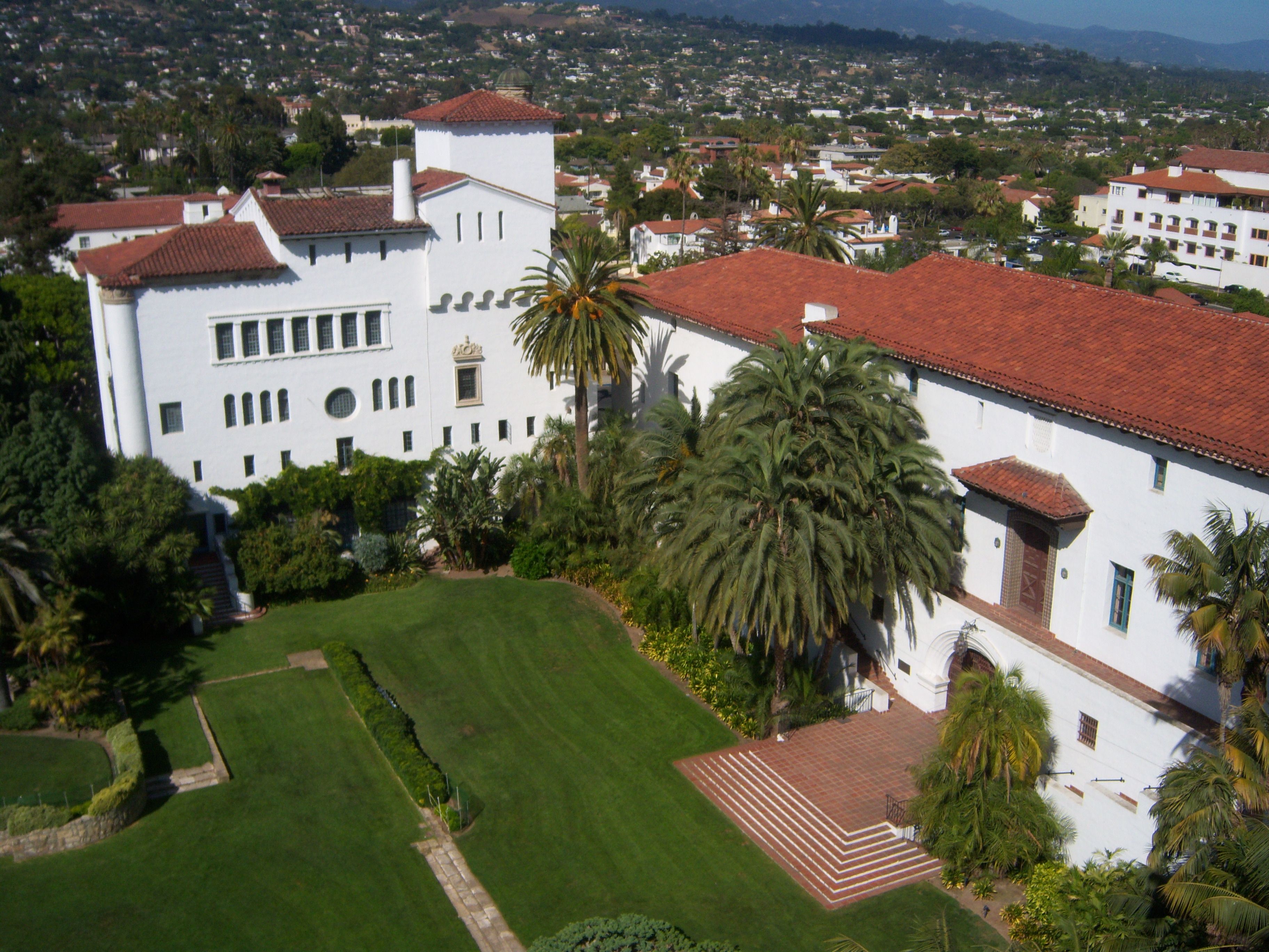 The Birds eye view of the Santa Barbara courthouse, with its white stcco walls, red tile roof, verdant grounds, and the city in the background.