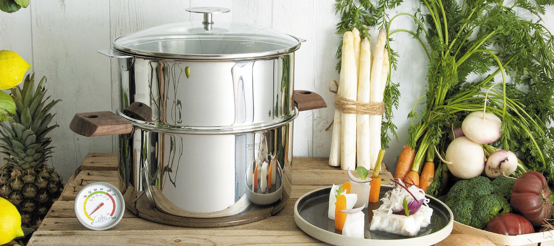 A luxury stainless steel double-deck steam pot with lid, displayed among an assortment of fresh vegetables