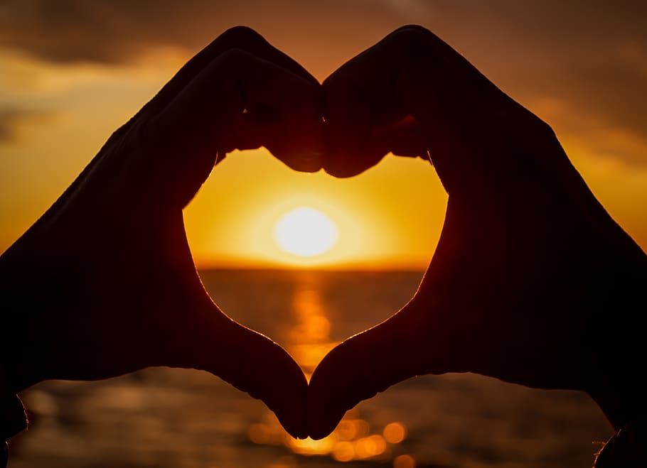 Hands making a heart shape over the sun setting over the ocean
