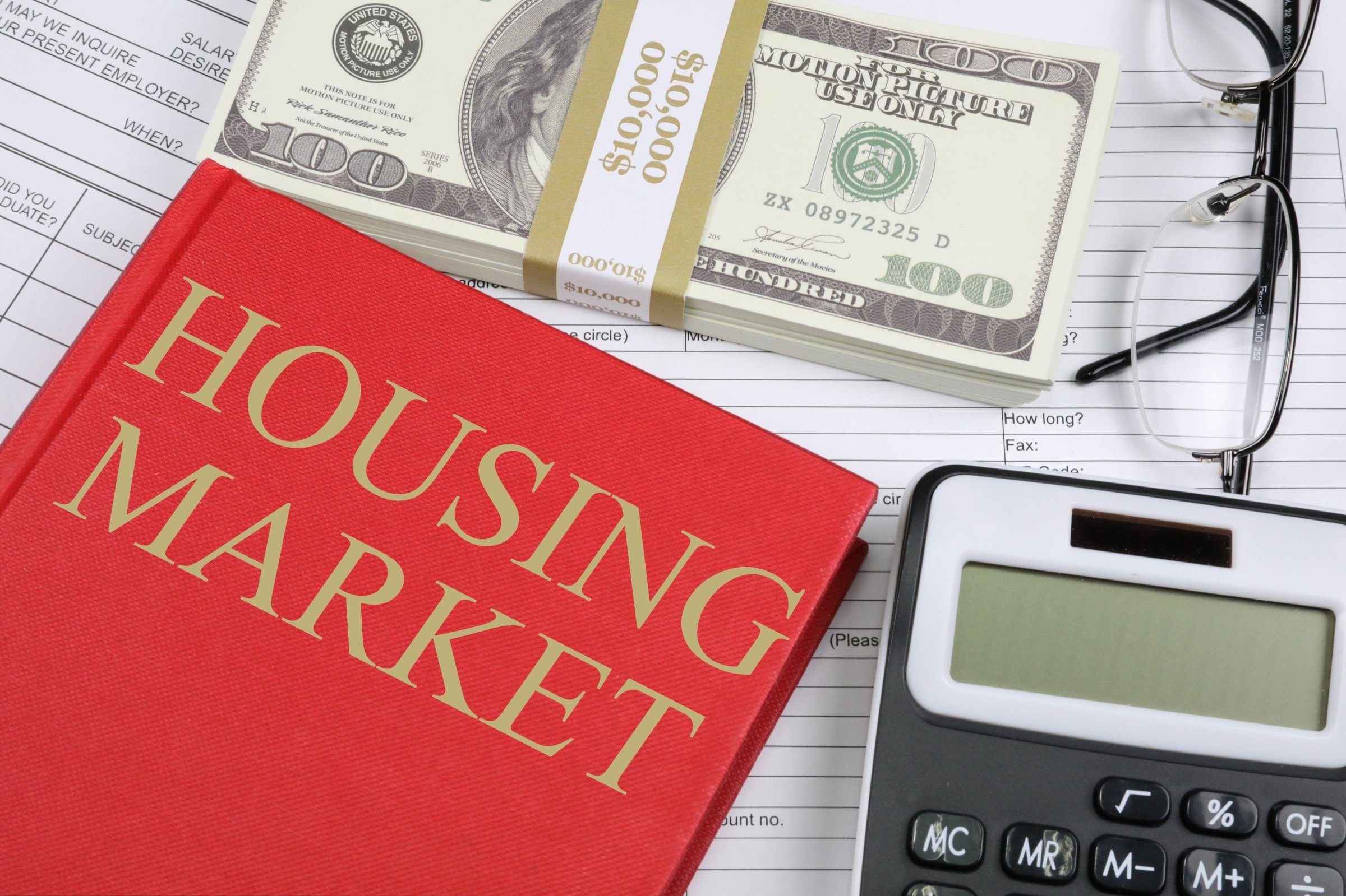 A red book titled Housing Market next to a calculator and other papsers.