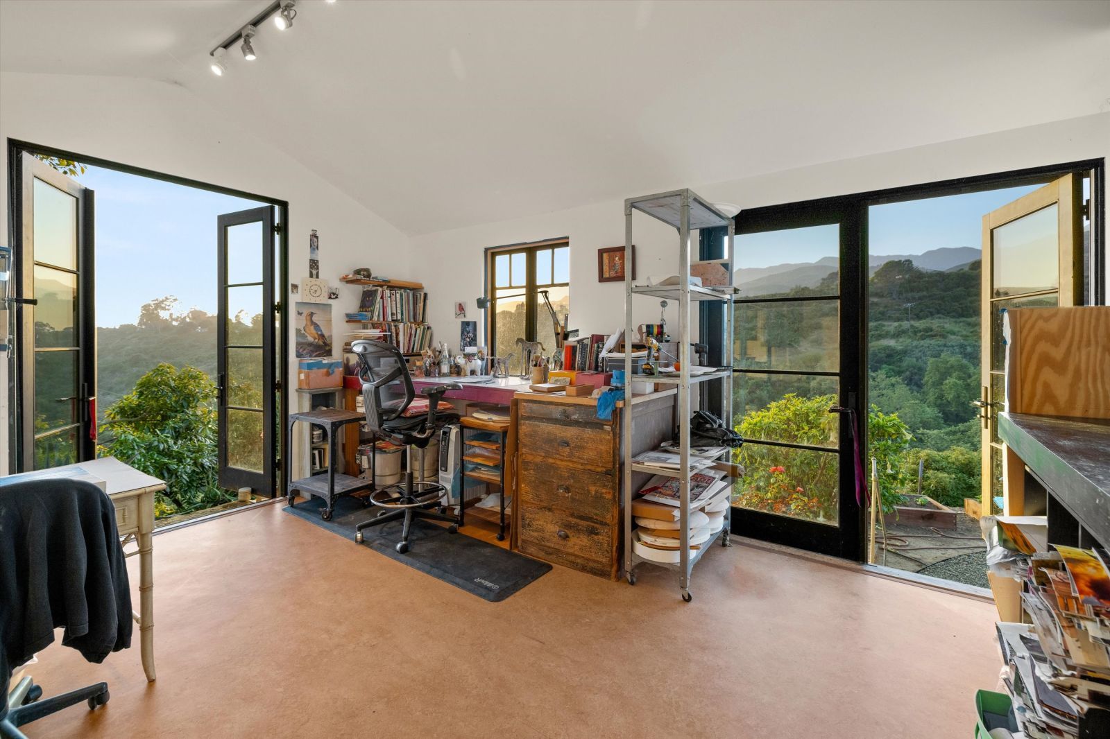 A room with a desk and a pair of large glass French doors looking out to the gardens