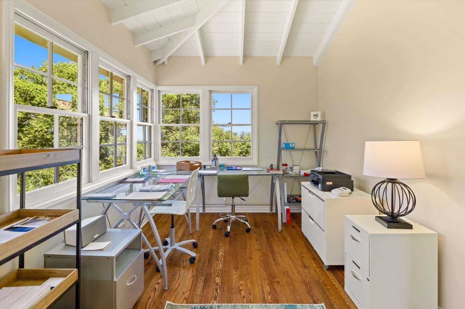 A bright white home office with a desk and cabinets, and several large windows looking out to trees