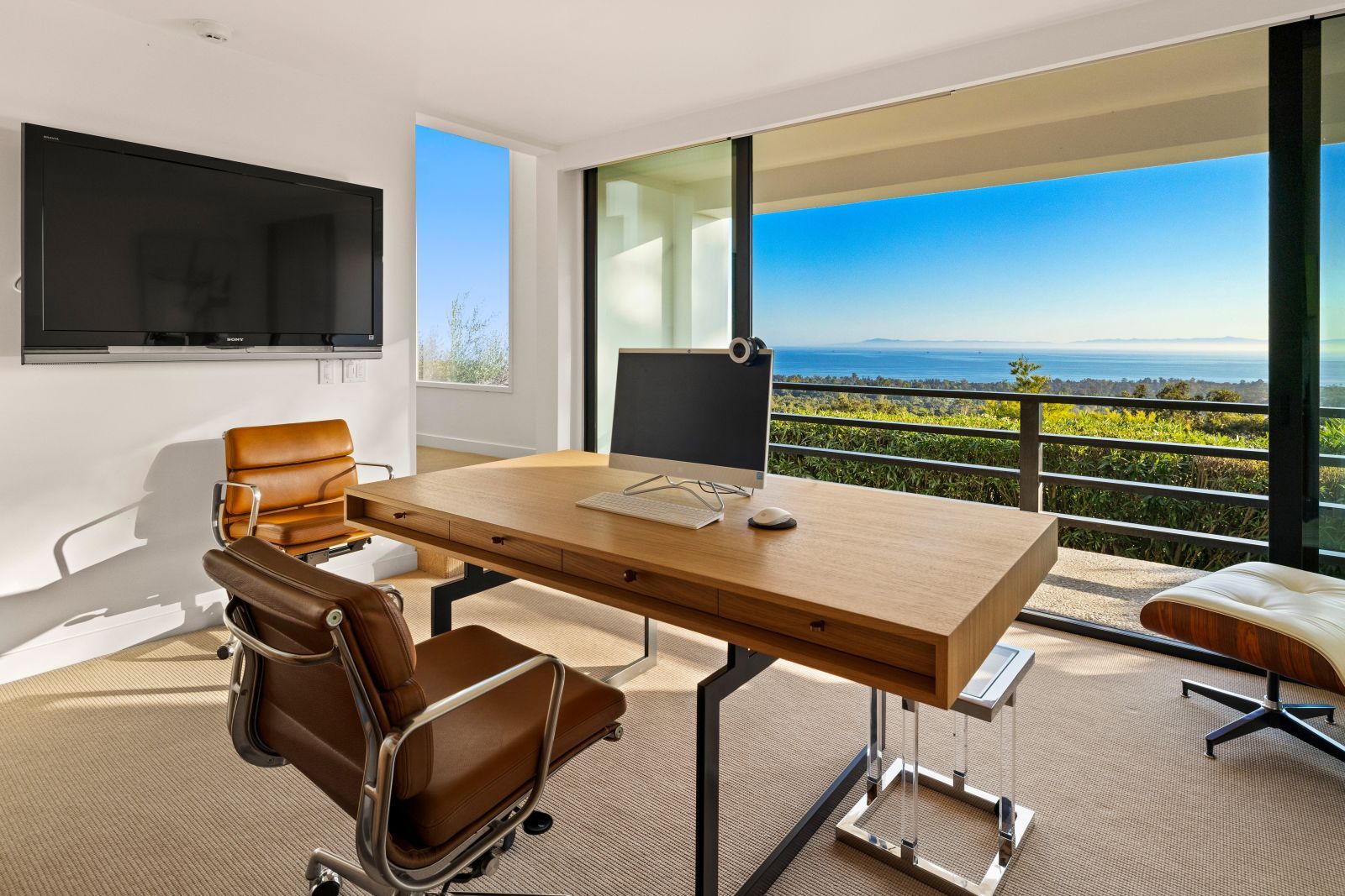 A desk with a computer and a chair in a room with a view of the ocean