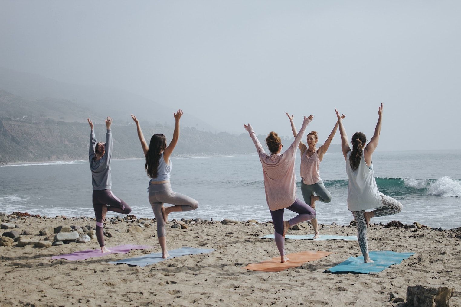 a group of 5 women doing Yoga on a foggy beach beach