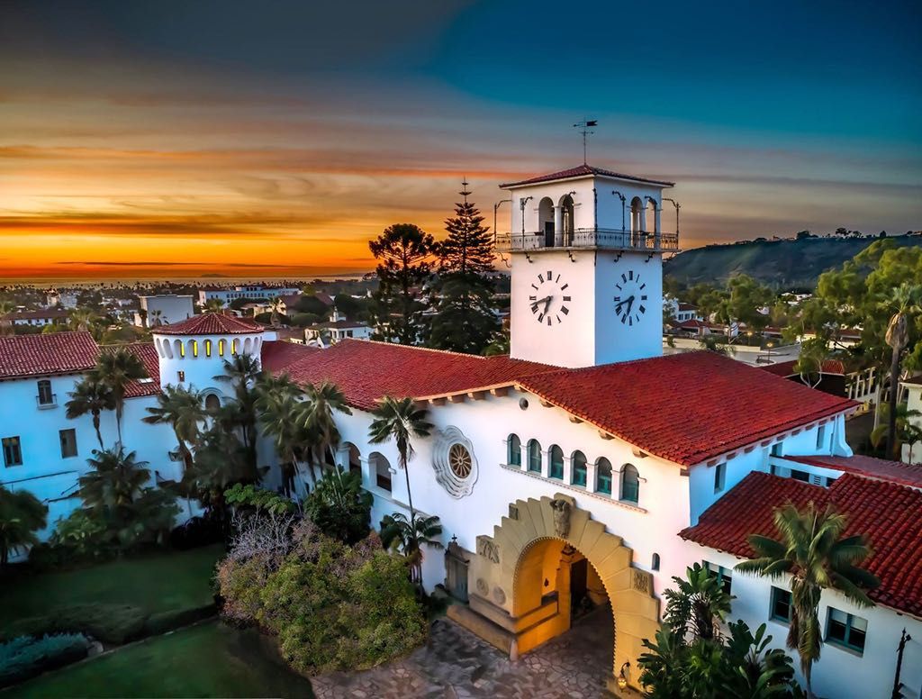 Sunset drone photo of the picturesque Spanish Colonial Revival Santa Barbara courthouse, with Santa Barbara and the sunset in the background