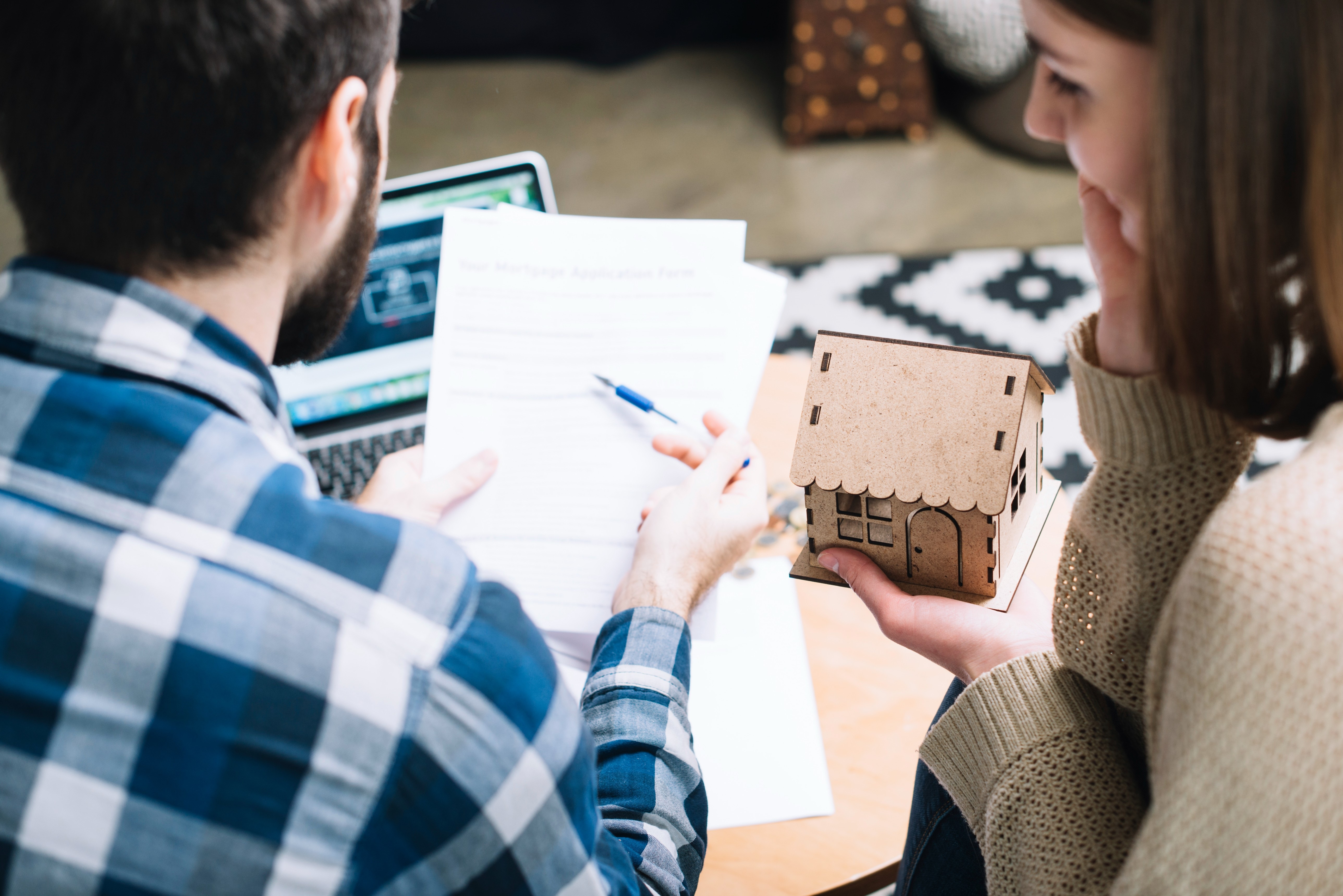 Homebuyers reviewing paperwork and discussing a real estate offer while holding a model house, representing a clean and competitive home purchase strategy.