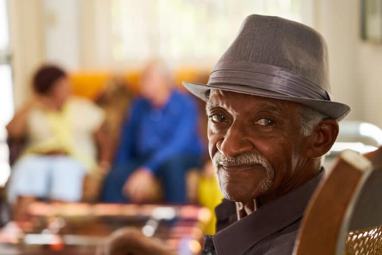 elderly man wearing a hat sitting in a chair smiling