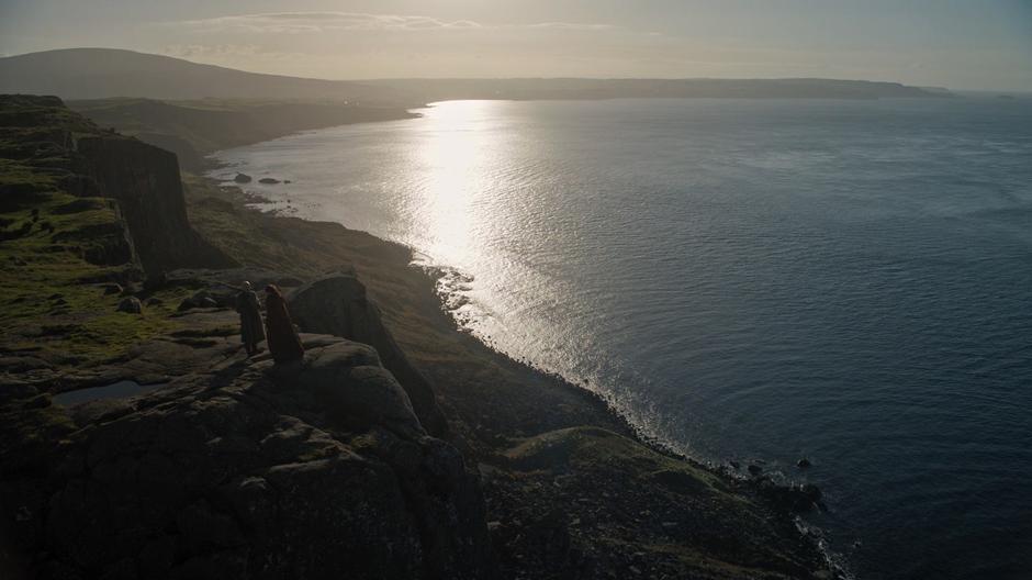 Varys and Melisandre chat on the cliffs above the path.