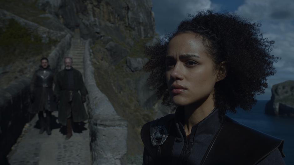 Missandei stands at the corner looking out over the sea while Jon and Davos approach her from up the stairs.