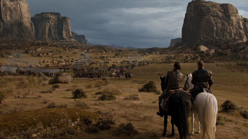 Bronn and Jaime sit on their horses watching the Lannister forces mingle around the lake.