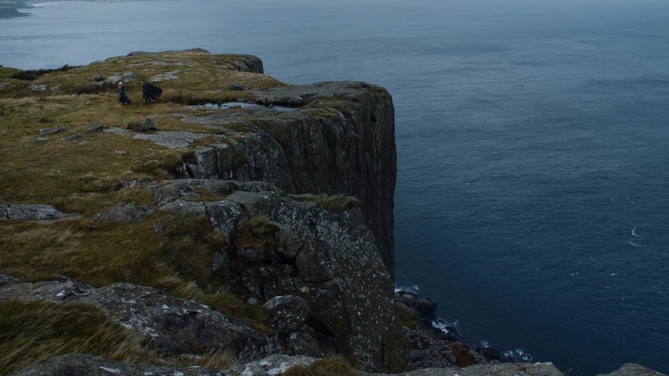 Daenerys and Jon walk away from the cliff edge while chatting.