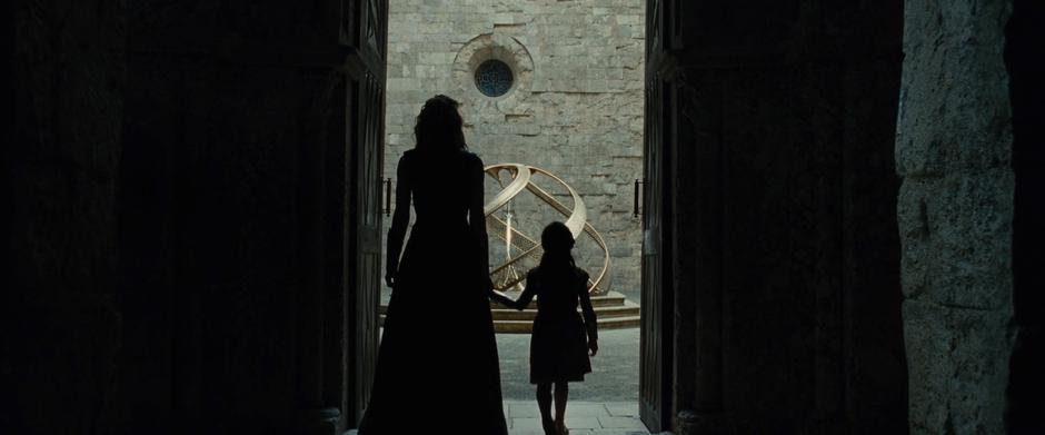 Hippolyta and young Diana walk into the center of the tower holding hands.