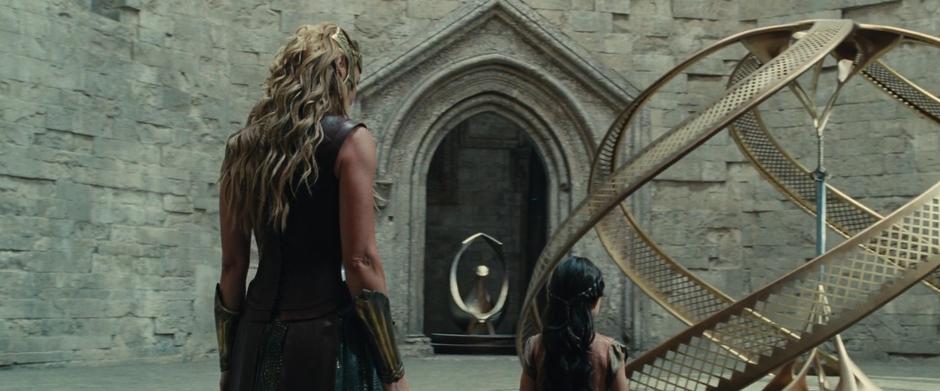 Young Diana approaches the sword's stand while her mother watches.