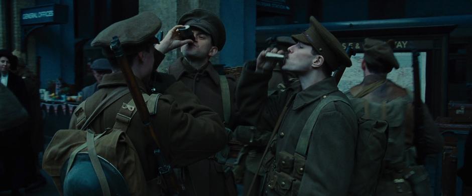 Three soldiers take a drink from their flasks.