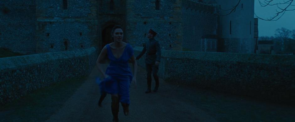 Diana runs towards the village as Steve looks up at the roof where the canon shot the weapon from.