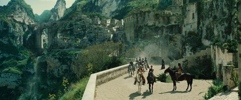 Diana rides on a horse with her mother while Antiope rides next to them and a number of Amazons follow behind.