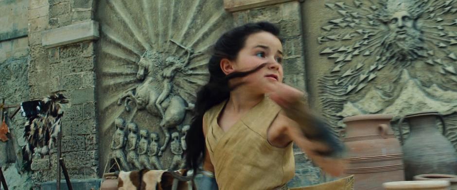 Diana looks behind her while running past some stone carvings.