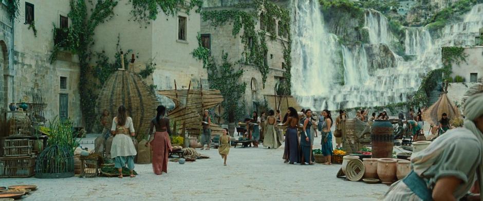 Various Amazons turn to watch as young Diana runs through the market.