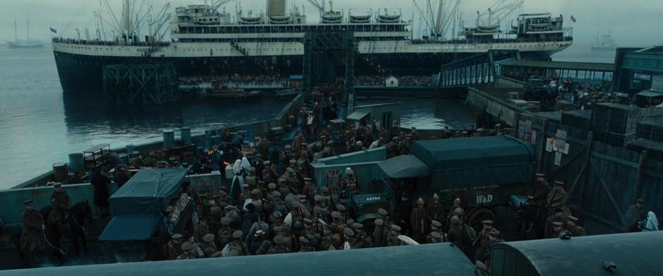 Soldiers swarm the dock heading to and from the large ship docked in the river.