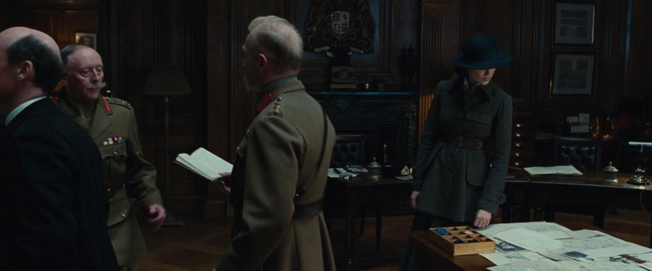 Diana looks at the documents on the table while the military commanders examine the notebook.