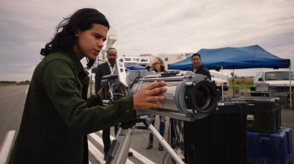 Cisco lovingly strokes his Speed Force Bazooka while Joe, Caitlin and Wally watch.