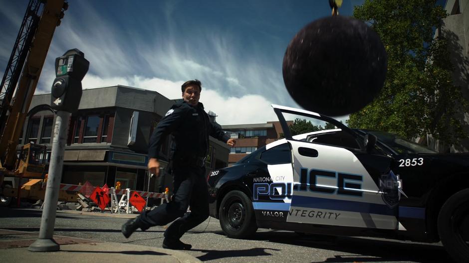 A police officer dives away as the wrecking ball crashes down on his squad car.