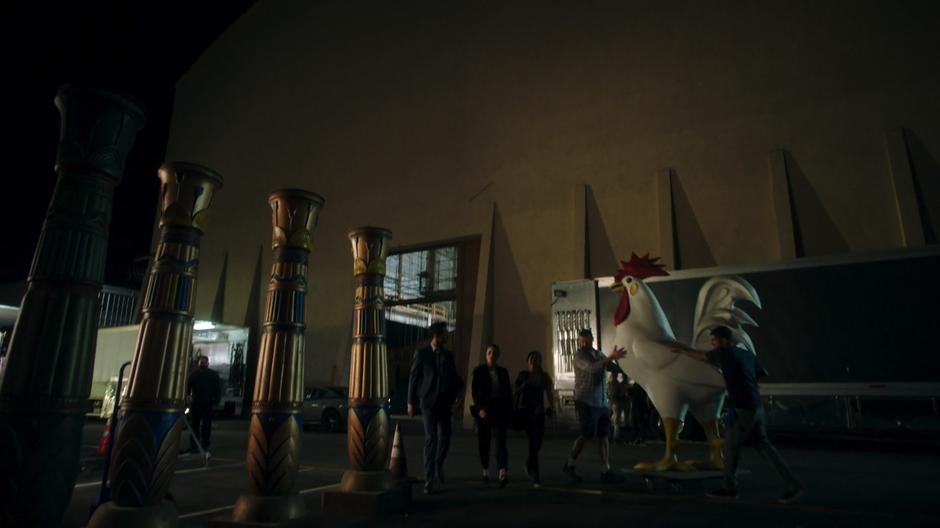 Lucifer, Chloe, and Ella watch across the studio lot to the sound stage.