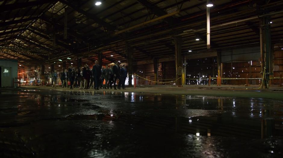 Oliver leads the Markovian executives and the reporters on a tour of the abandoned factory.