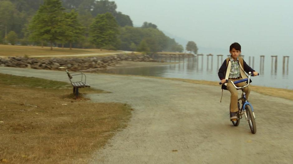 Young Ray rides his bike on a path by the water.