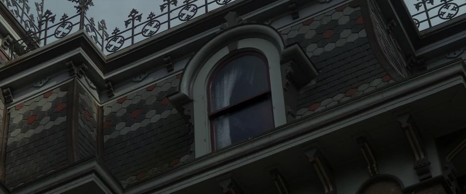 A mysterious figure looks down from a window high on the front of the mansion.
