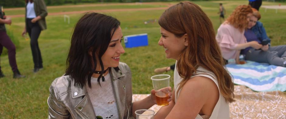 Carmilla and Laura look at each other while sharing a drink and the rest of the gang talks in groups behind them.