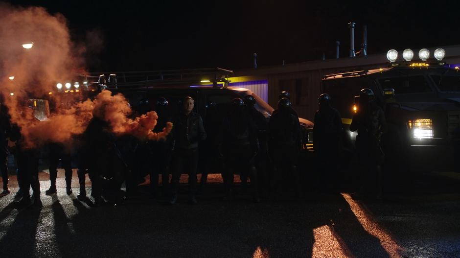 Mr. Priest holds a smoking smoke grenade next to a line of other guards.