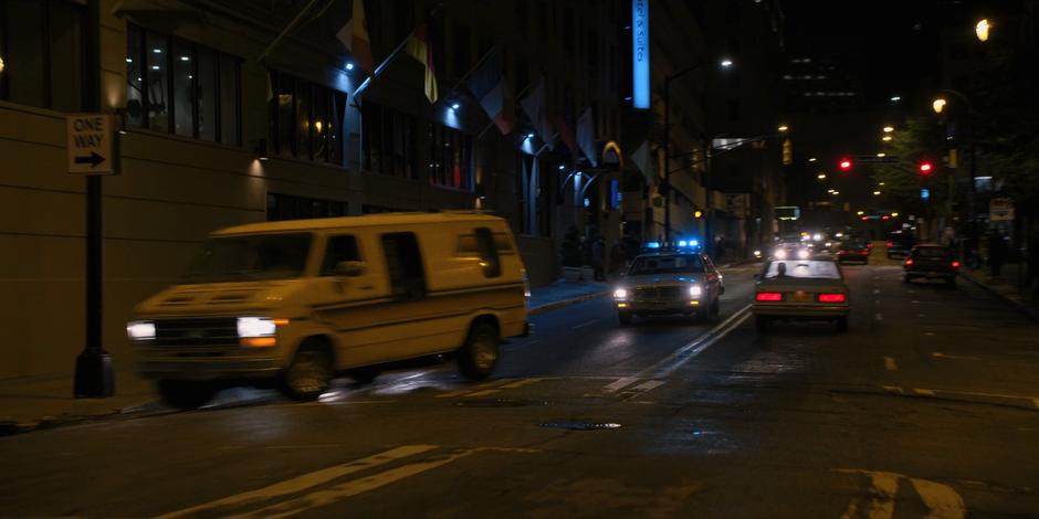 The van turns the corner onto a one-way street followed closely by the cop car.