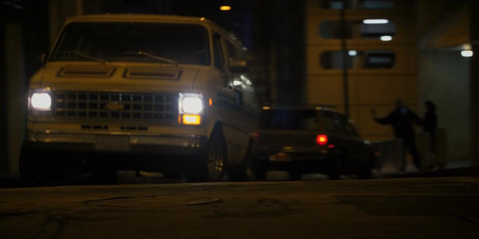 The van barrels down the alley while a car behind it turns and blocks the way.