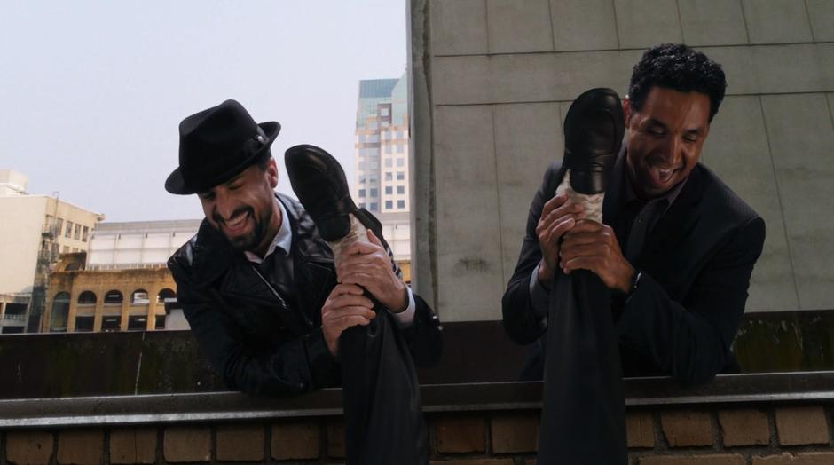 Two goons hold Ralph Dibny over the edge of the building by his legs.