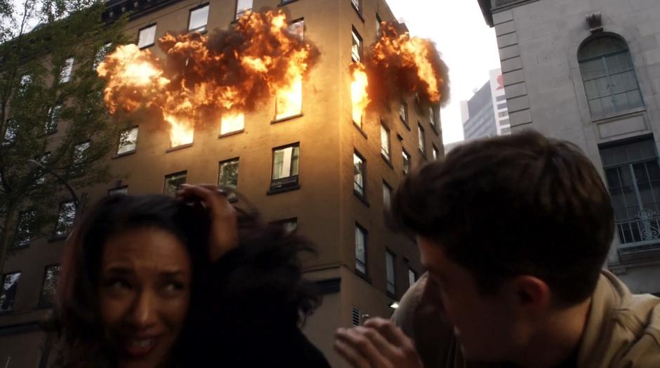 Iris and Barry duck to the ground as Ralph Dibny's office explodes.