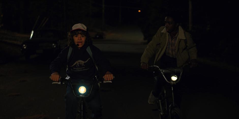 Dustin and Lucas bike down the road at night.