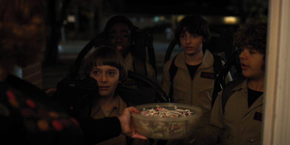 Will, Lucas, Mike, and Dustin look at the woman as she offers them candy after mistaking their costumes for normal exterminators.