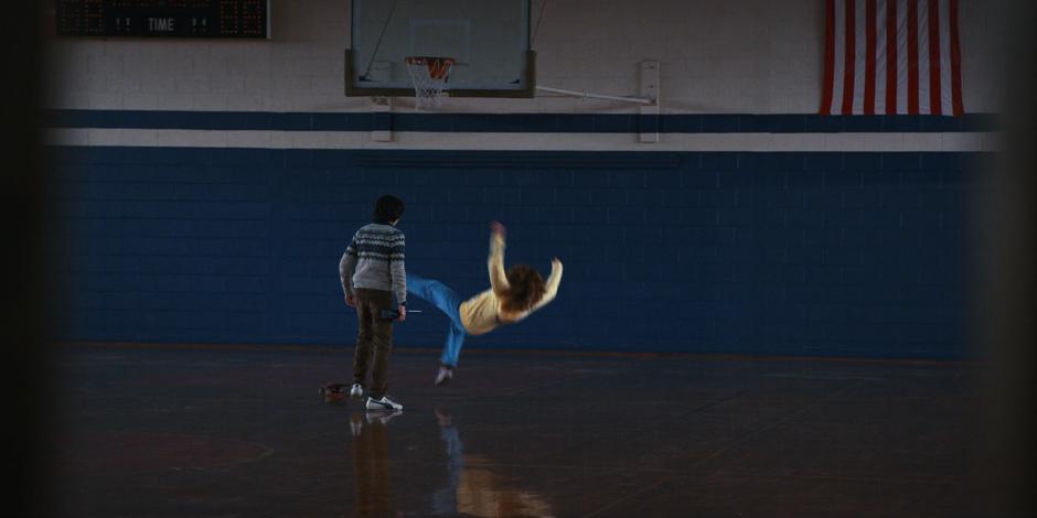 Mike watches as Max's skateboard flies out from under her and she falls to the floor of the gym.