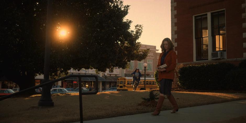 Dustin bikes around the corner of the library as someone walks away with a stack of books.