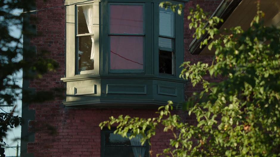 The Vigilante points his gun out of the window of the nearby building.