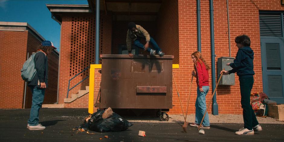 Lucas jumps out of the dumpster where he is searching for Dart with Max & Mike as Dustin comes up.