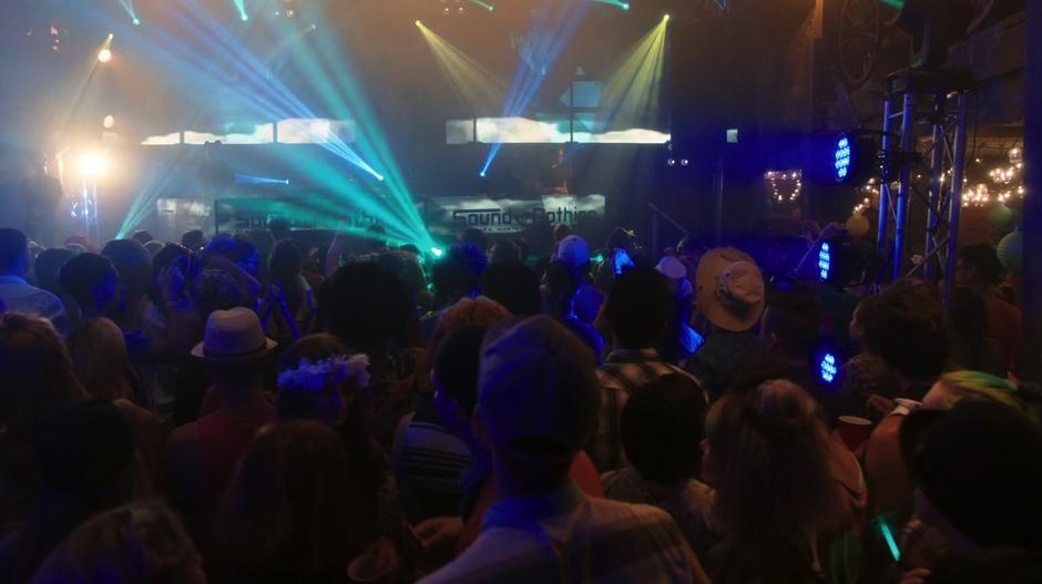 People crowd on the dance floor in front of the stage while lights shine around the room.