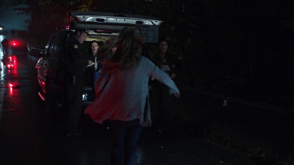 Eliza runs up to Alex and Kara who are sitting in the back of police SUV.