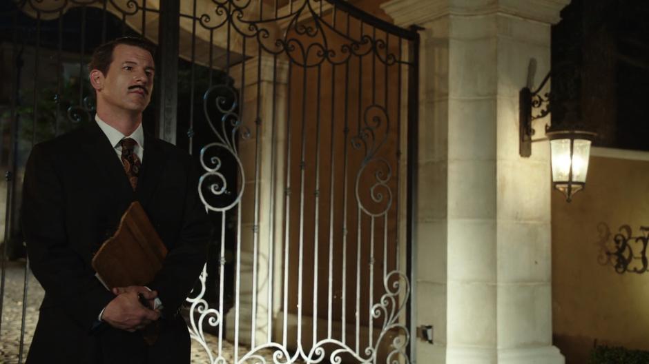 A man with a clipboard stands at the gate of the mansion.