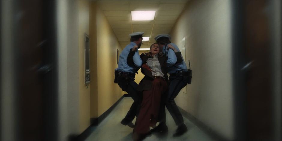 Two security guards drag Terry Ives down the hallway.