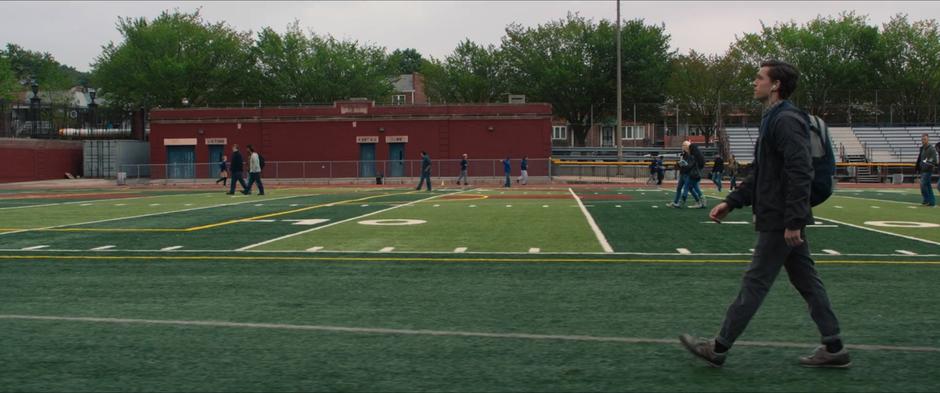 Peter walks across the football field while listening to music.